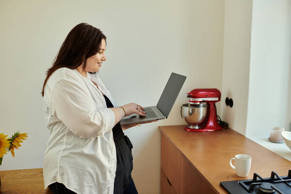 Веселая женщина с ноутбуком в уютной обстановке на кухне.