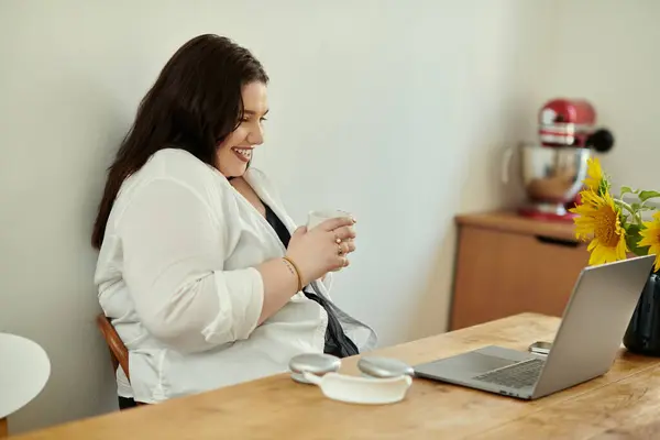 stock image Plus size woman smiles while sipping a drink at her cozy home workspace.