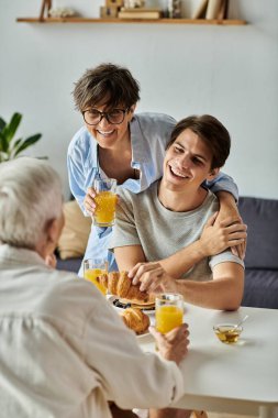 Lezbiyen ebeveynler ve yetişkin oğulları tarafından paylaşılan sıcak bir kahvaltı anı, kahkaha ve sevgiyle dolu..