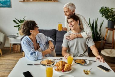 Sevgi dolu bir aile kahvaltıdan zevk alır, kahkahaları ve sıcaklığı paylaşır, içeceklerini yudumlar ve lezzetli yemekler yerler..