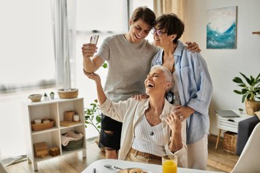 Loving lesbian parents and their adult son relish quality time and laughter over breakfast in their bright home. clipart