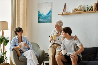 Lezbiyen ebeveynler ve yetişkin oğulları sıcak bir ortamda sıcak içecekleri yudumlarken aynı kahkahayı ve sevgiyi paylaşıyorlar..