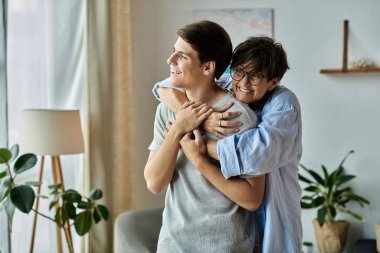 Neşeli bir anne oğlunu kucaklıyor, sıcak bir oturma odasında gülüşünü ve sevgisini paylaşıyor..