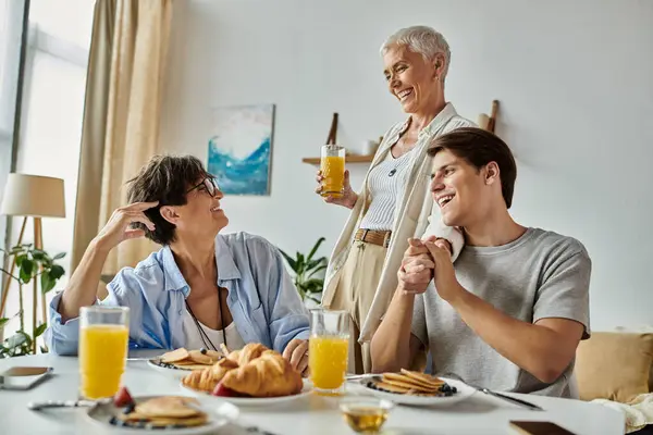 stock image Three family members share laughter and delicious breakfast in a sunlit, welcoming kitchen.