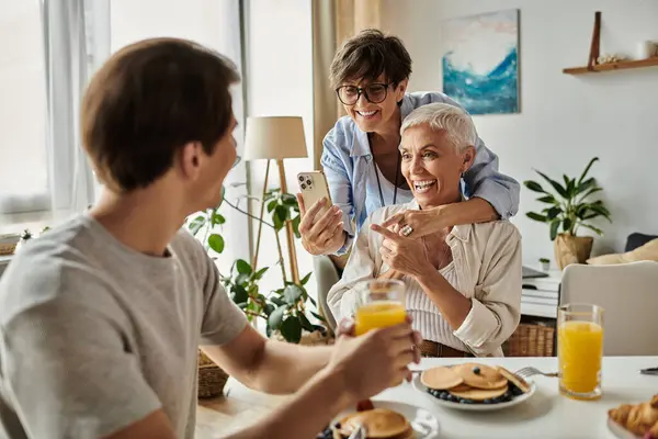 stock image Lesbian parents and their adult son share a cheerful breakfast moment, enjoying laughter and connection.