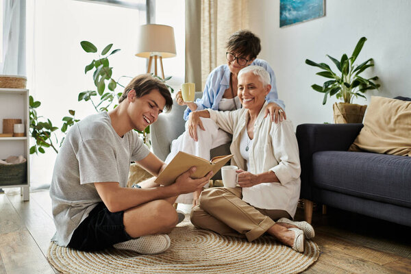Родители-лесбиянки с любовью поддерживают своего взрослого сына, когда он читает, окруженный теплом и смехом.