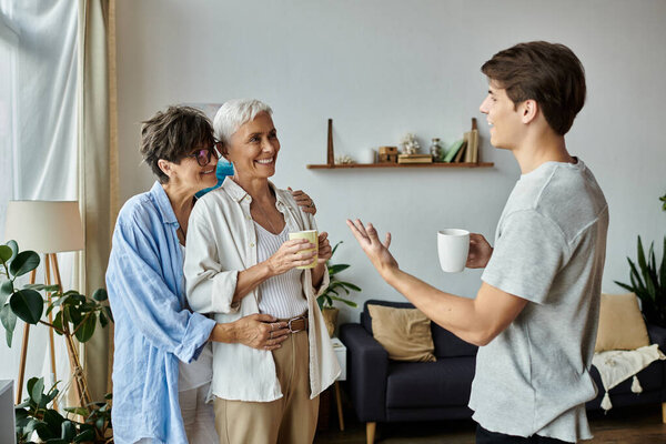 Родители-лесбиянки и их взрослый сын делятся смехом и историями, наслаждаясь кофе вместе.