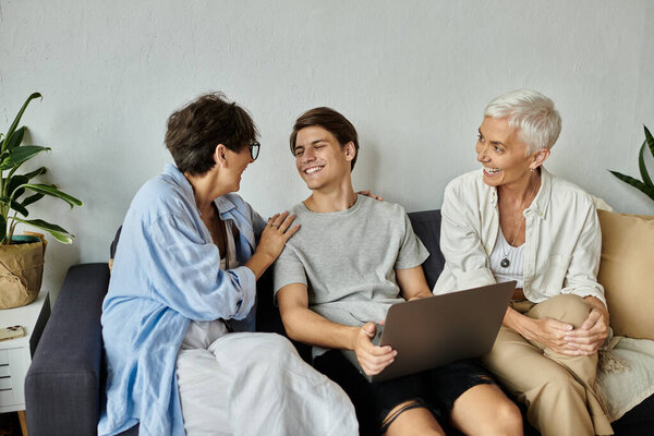 Родители-лесбиянки и их взрослый сын делят радостные моменты отдыха на диване дома.