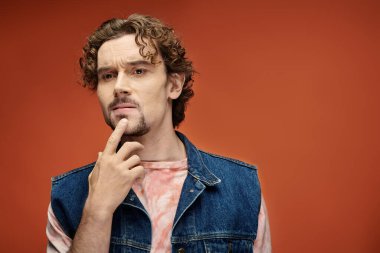 Contemplative man with curly hair poses thoughtfully against a rich orange background. clipart