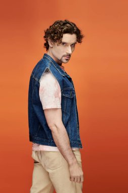 Çarpıcı bir adam canlı turuncu bir zemin ile düşünceli poz verir..