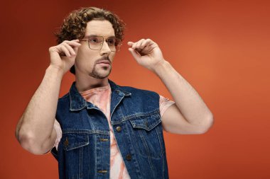 Yakışıklı bir adam gözlüklerini ayarlar, derin duygularını renkli bir arkaplana aktarır..