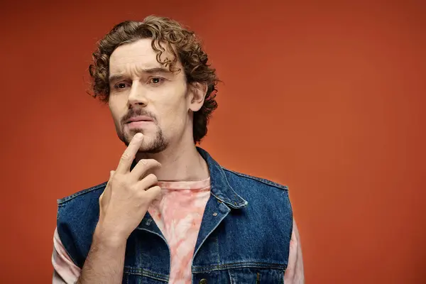 stock image Contemplative man with curly hair poses thoughtfully against a rich orange background.