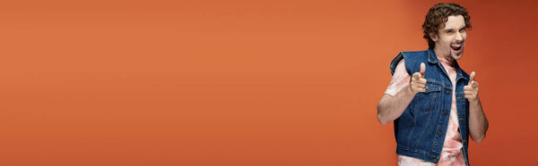 Стильный мужчина выражает харизму игривым жестом в яркой обстановке.