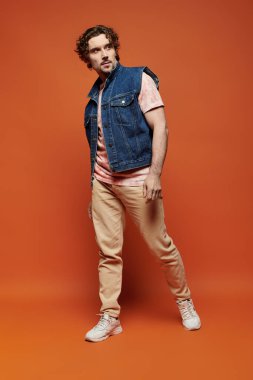 Şık bir adam canlı turuncu bir arka planda duygusal poz verir..