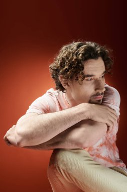 Düşünceli bir adam dizlerini canlı bir arka planla sarıp ifadesini güçlendirir..