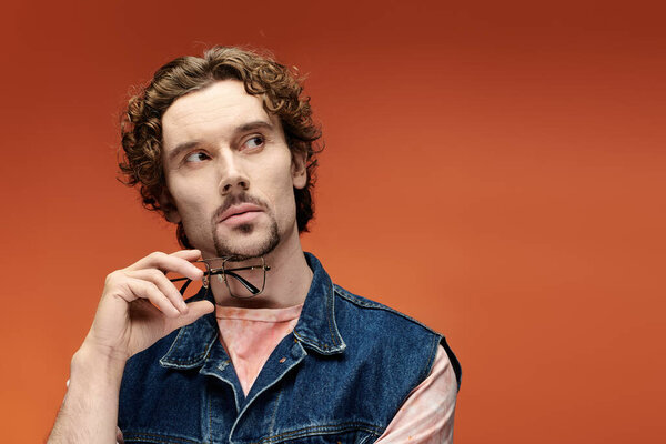 Красивый мужчина задумчиво позирует на ярком оранжевом фоне.