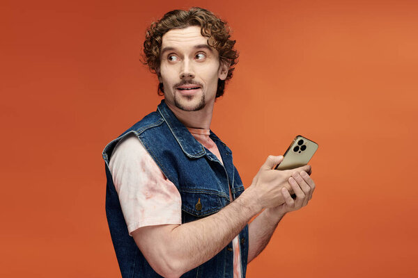 Мужчина с вьющимися волосами взволнованно держит телефон, демонстрируя свое очаровательное выражение.
