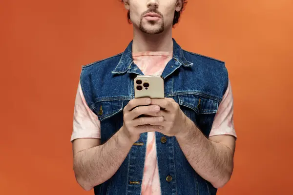 stock image Handsome man expresses emotions while holding a smartphone before a vivid backdrop.