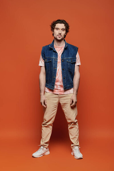 Красивый мужчина задумчиво позирует на ярком оранжевом фоне..