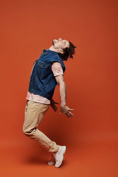 Человек радостно позирует с распростертыми объятьями на ярко-оранжевом фоне.