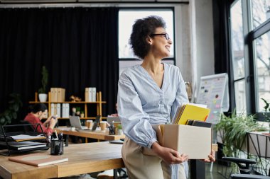 Attractive african american woman packing her items during lay off, colleagues on backdrop. clipart