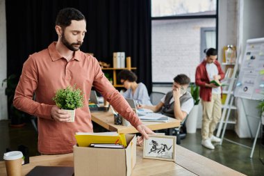 Exquisite man packing his items during lay off, colleagues on backdrop. clipart