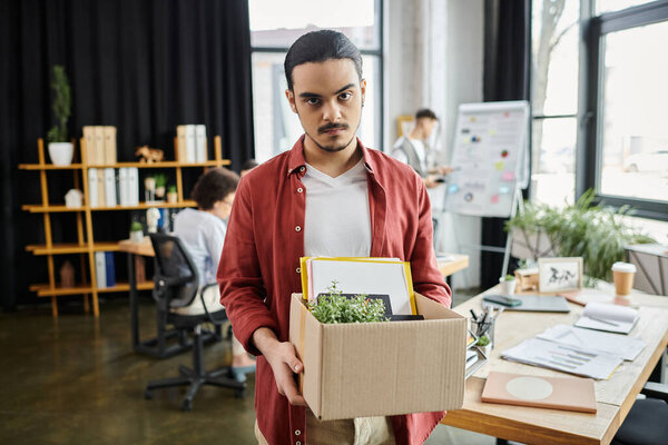 Professional pack belongings amidst an emotional workplace transition, with colleagues on backdrop.