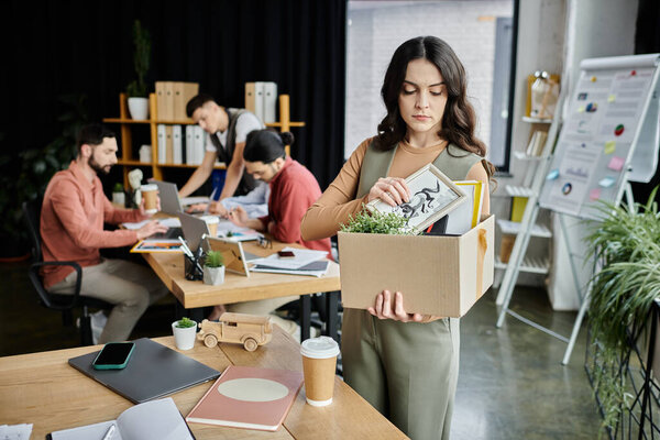 Good-looking woman handle belongings during a challenging time at work, colleagues on backdrop.
