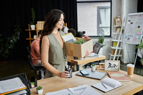 Woman reflect on changes while packing personal items, colleagues on backdrop.