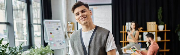 Young jolly man during lay off, colleagues on backdrop.