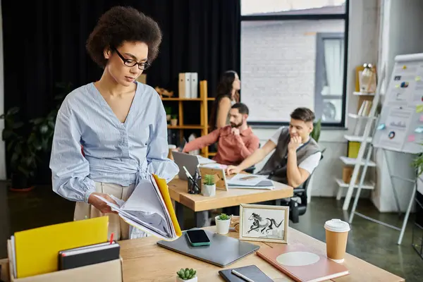 stock image Chic african american woman packing her items during lay off, colleagues on backdrop.