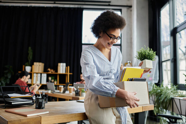 Young african american woman packing her items during lay off, colleagues on backdrop.