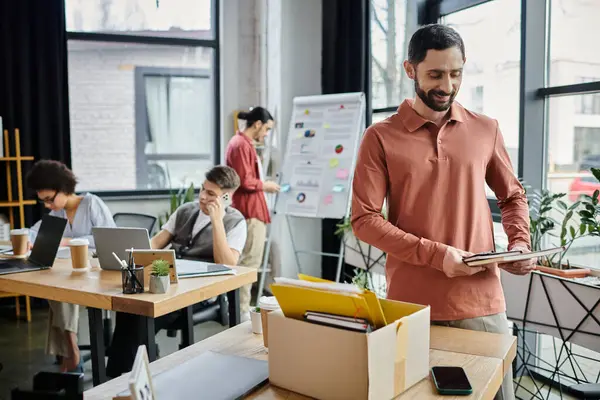 stock image Cheerful man packing his items during lay off, colleagues on backdrop.