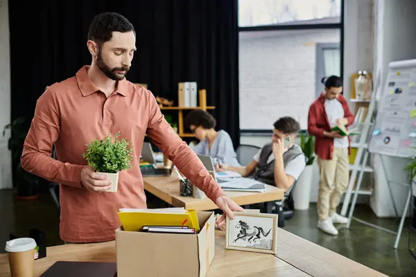 Stock image Exquisite man packing his items during lay off, colleagues on backdrop.