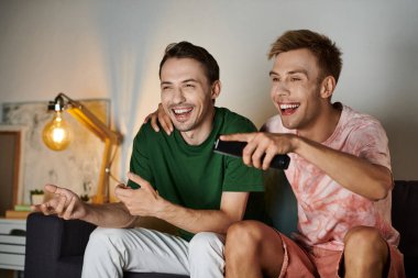 İki adam kanepede dinlenirken gülüşlerini ve gülüşlerini paylaşıyor..