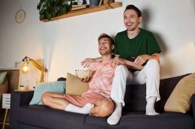 Two men enjoy a cozy night filled with laughter and snacks at home. clipart