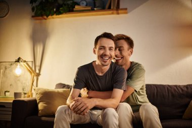 Two men embrace and laugh together in their warm, inviting living room. clipart