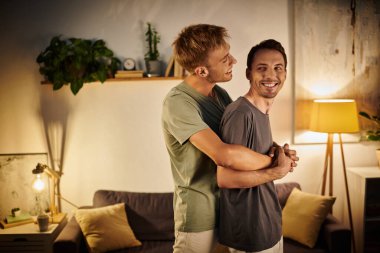 İki erkek evde eğlenirken birbirlerine sımsıkı sarılırlar..