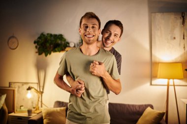 İki erkek, oturma odalarında kucaklaşırken keyifli bir anı paylaşıyor..