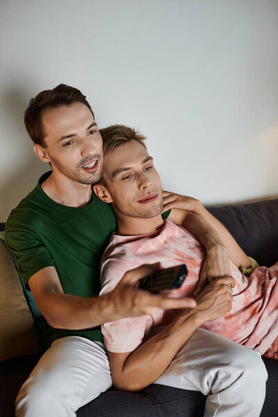 Two men enjoying each other on the couch while watching TV at home.