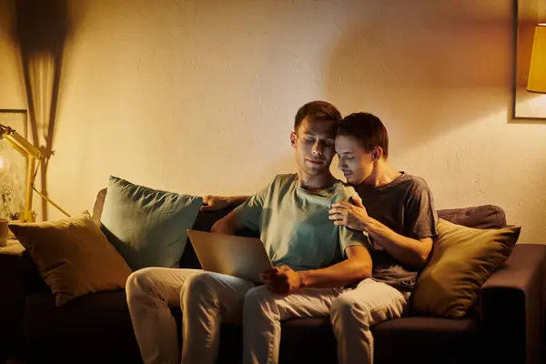 stock image Two men enjoy a warm moment together while using a laptop on the couch.