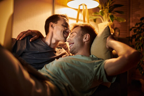 Двое мужчин радостно делятся нежными моментами вместе в своей гостиной.