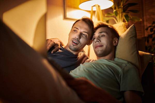 Двое мужчин разделяют теплый момент, расслабляясь на диване.