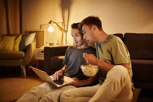 stock image Two men share laughs and popcorn while watching something on a laptop.