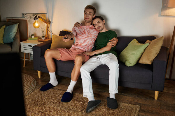 Двое мужчин отдыхают вместе на диване, разделяя тихий момент в их доме.
