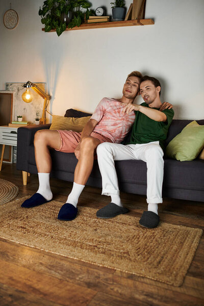 Двое мужчин разделяют нежный момент на своем уютном диване, купаясь друг в друге.