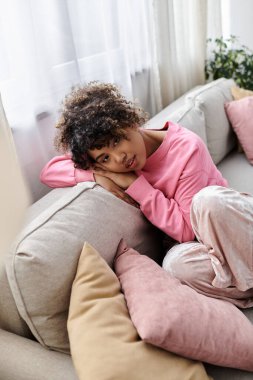 A young woman relaxes comfortably on the sofa at her home. clipart