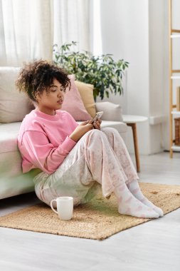 A young woman enjoys a peaceful moment at home, engrossed in her phone. clipart