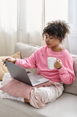 She sips coffee while working on her laptop, enjoying a cozy day at home. clipart