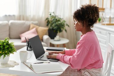 A beautiful woman focuses on her laptop while surrounded by home comforts. clipart